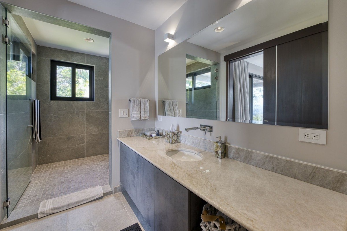 Bathroom has gray cabinets, marble countertop, and glass shower.