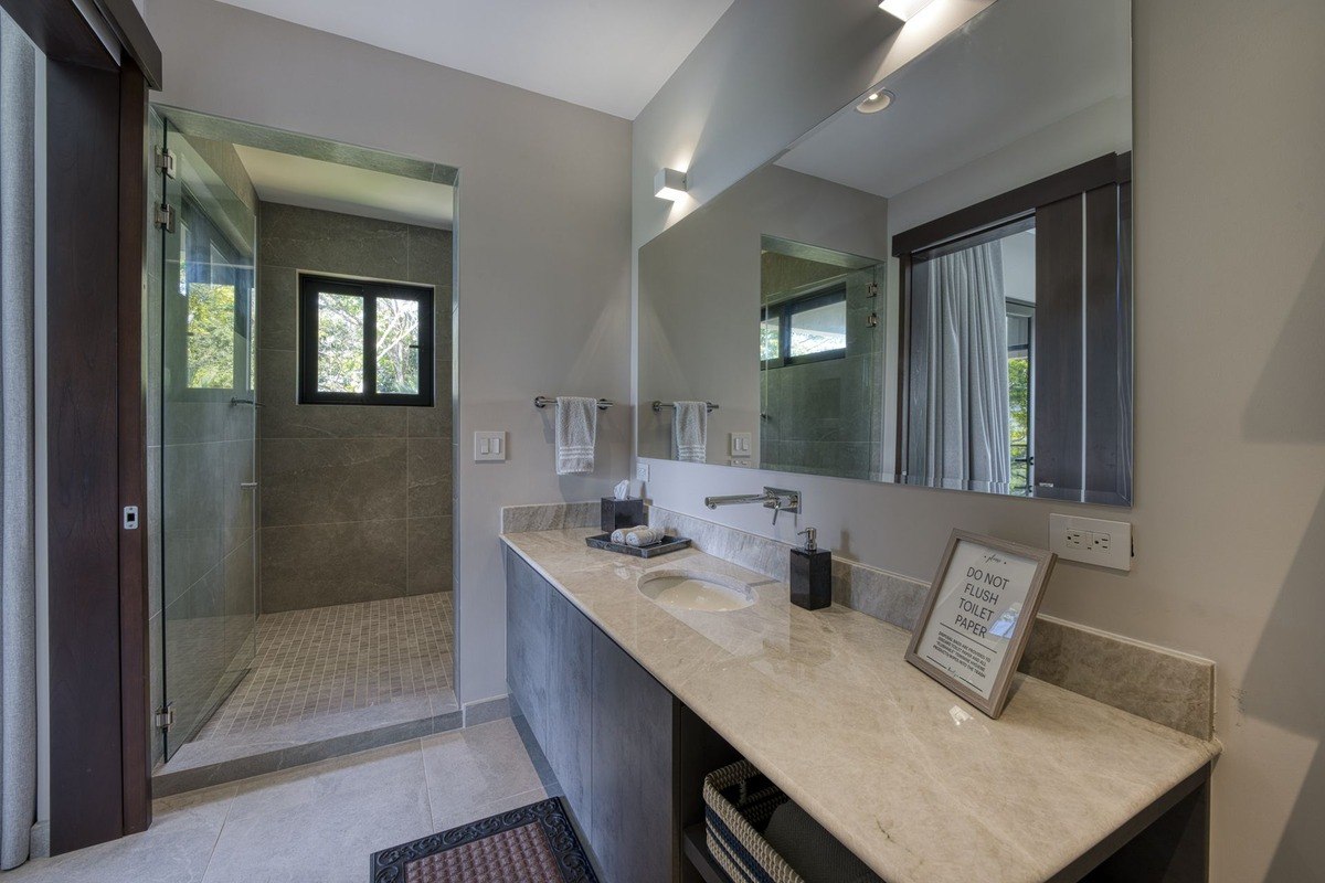 Bathroom has gray cabinets, marble countertop, and glass shower.