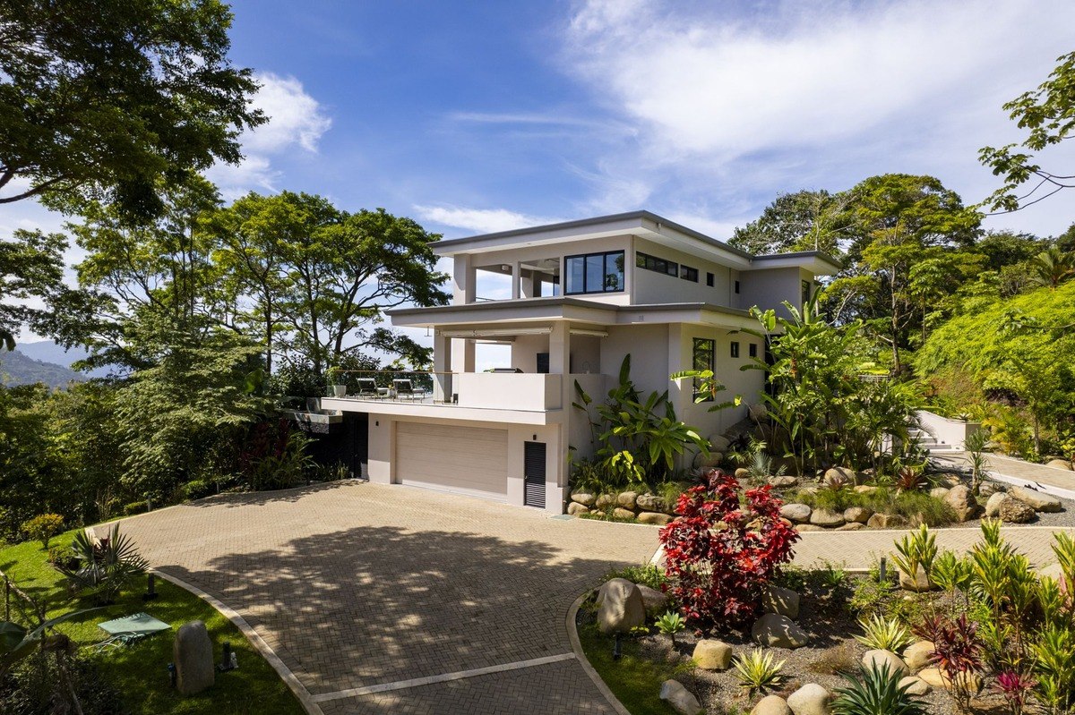 House has attached garage and is surrounded by tropical landscaping.