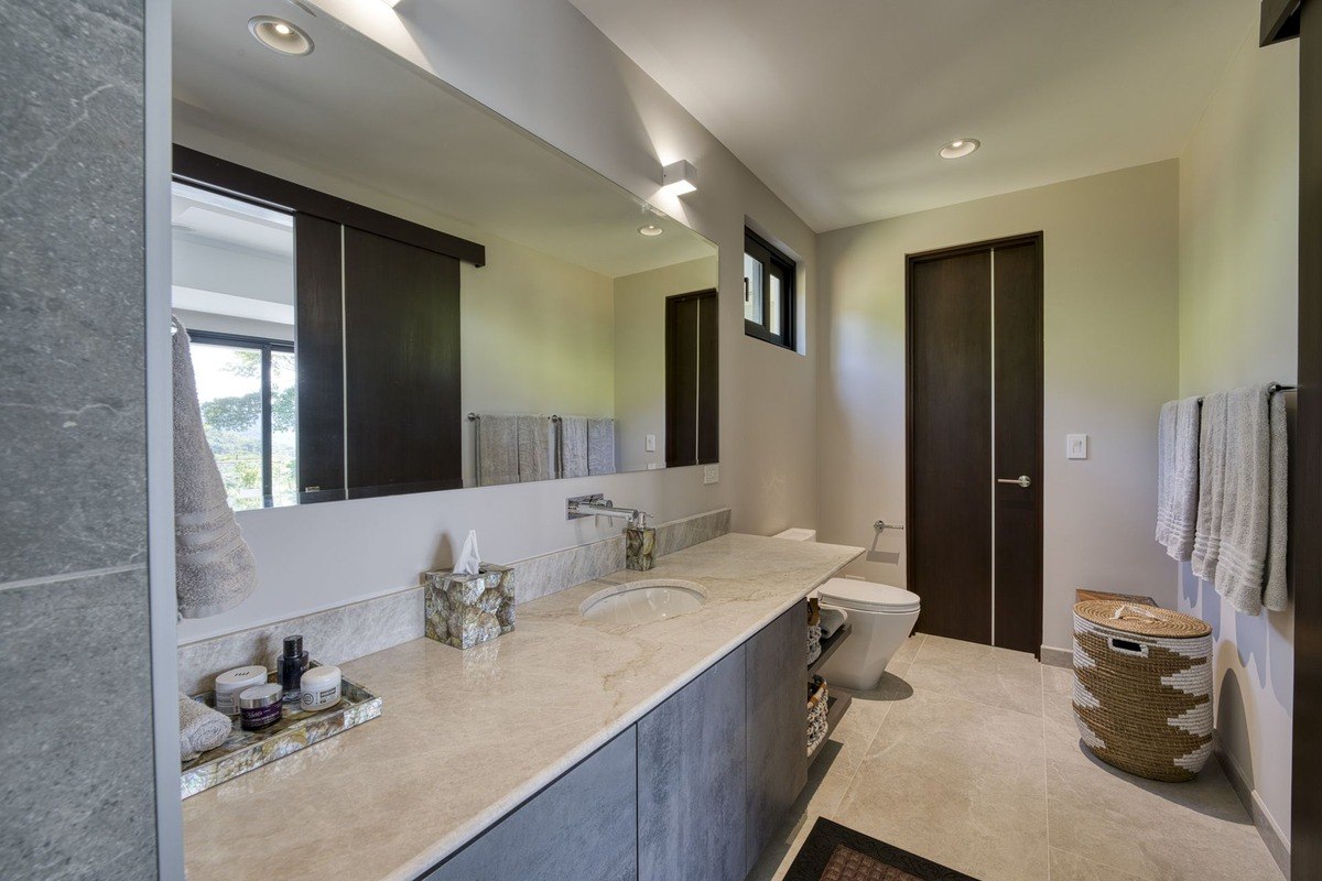 Bathroom has gray cabinets, marble countertop, and large mirror.