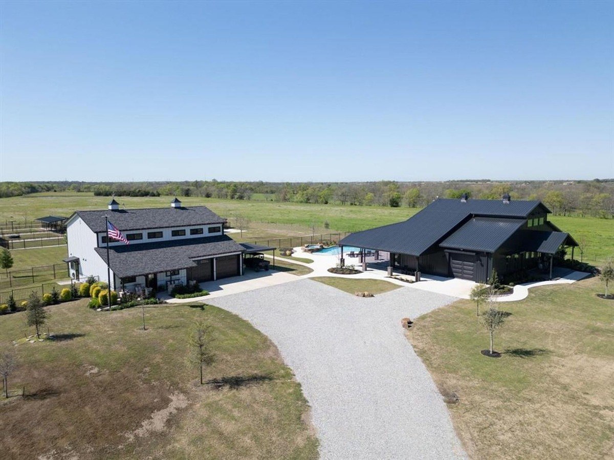 Rural property showcasing two large structures with a central driveway and open grasslands in the background.