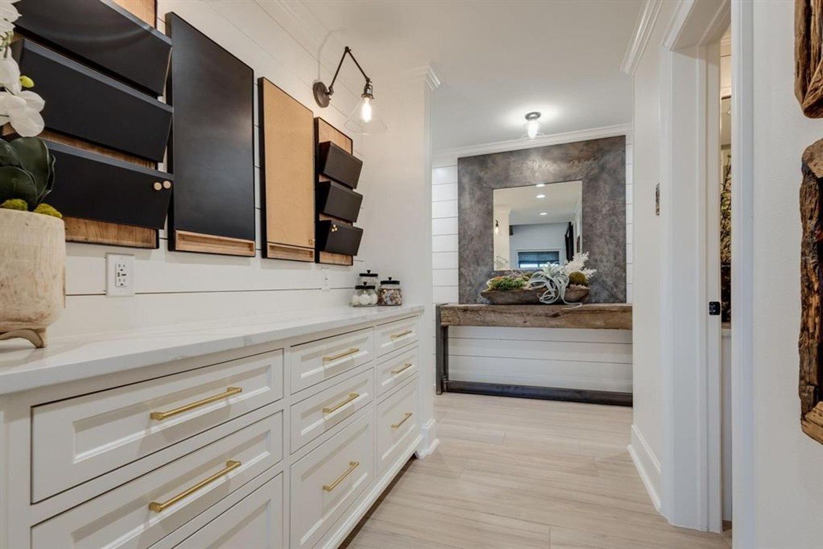 White cabinets with gold handles and sleek countertops create a modern workspace accented by a wall organizer system.