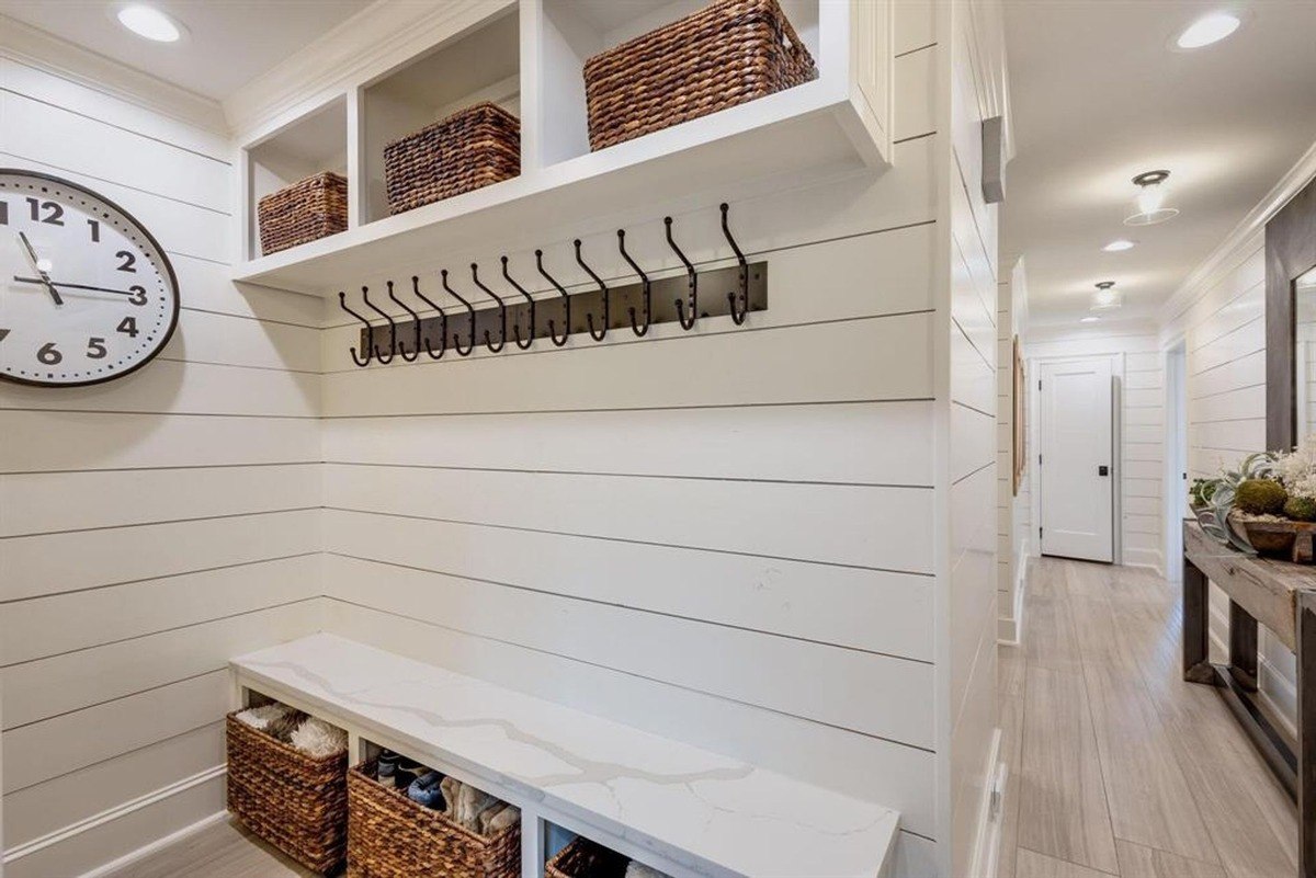 Mudroom features built-in storage with hooks, cubbies, and a cozy bench framed by clean shiplap walls.