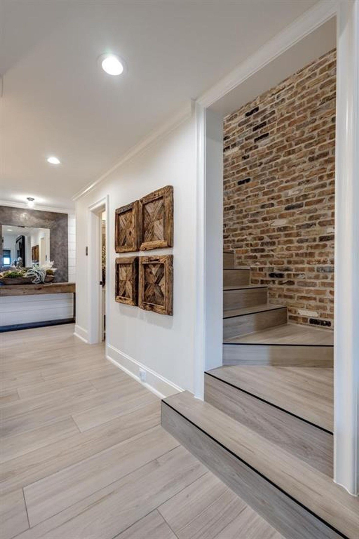 Rustic brick accent wall lines the staircase with neutral-toned wooden steps and decorative wall art.