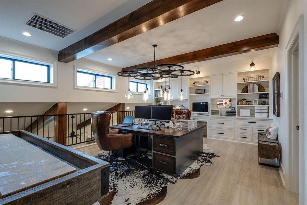 Spacious office with an industrial desk, exposed beams, and creative chandelier lighting designed with circular metal wheels.