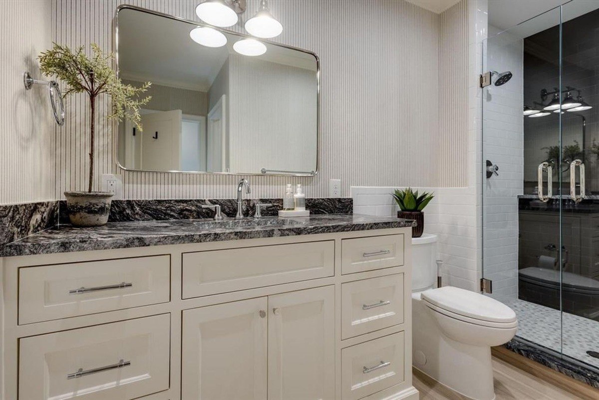 Black countertop with a textured mirror and decorative plants placed on white cabinetry.