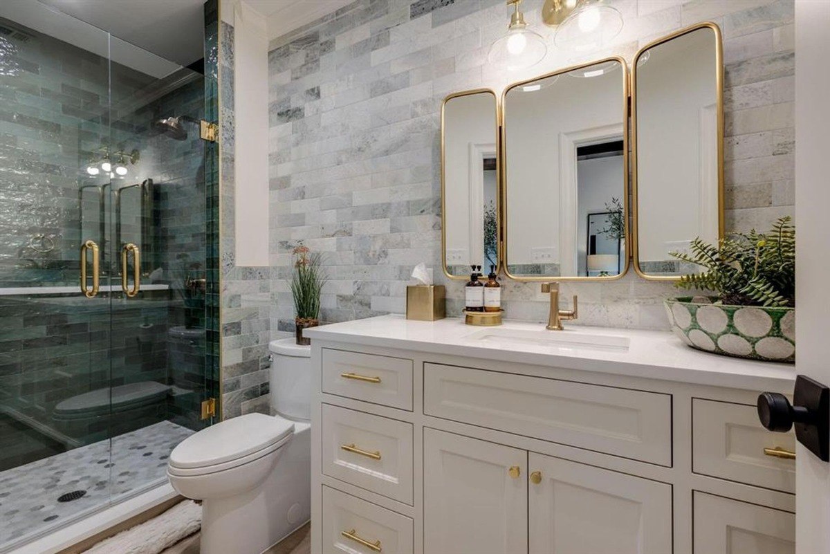 Bathroom featuring a glass-enclosed shower, gold fixtures, and white cabinetry.