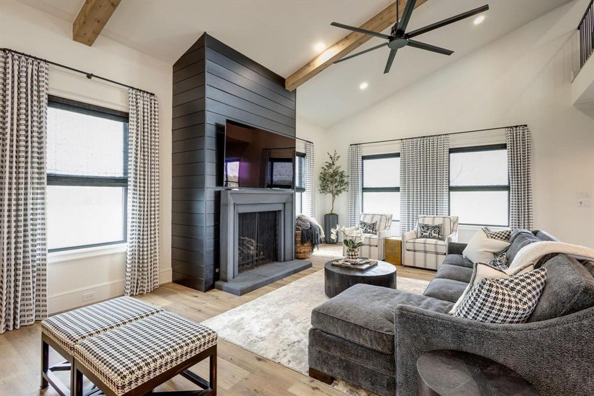 Living room with a dark shiplap fireplace wall, large sectional, and exposed beams enhancing the ceiling's design.