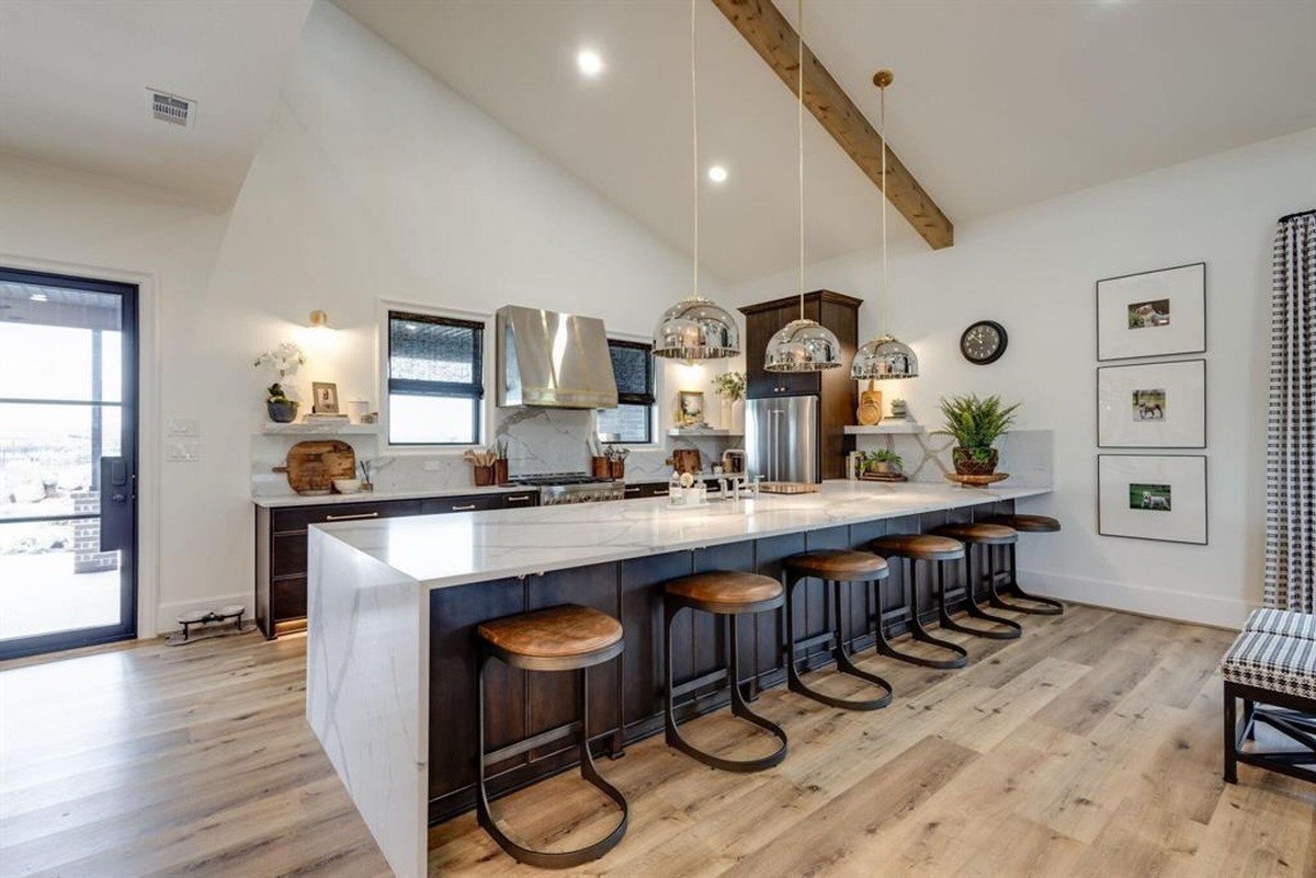 Bright kitchen featuring a long island with seating, metallic pendant lighting, and modern dark cabinetry.