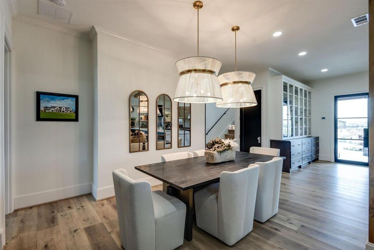 Elegant dining room centered around a dark table, light-up chandeliers, and wall mirrors with gold accents.