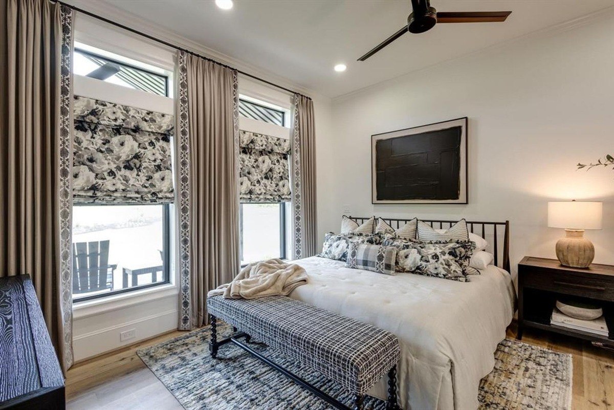 Comfortable bedroom with floral-patterned shades, layered bedding, and a bench placed at the foot of the bed.