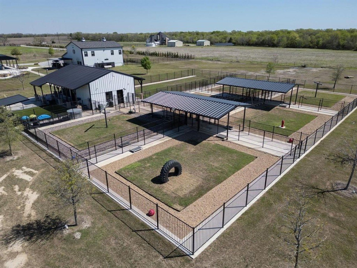 Fenced area designed as a dog park with shaded structures and open play zones.