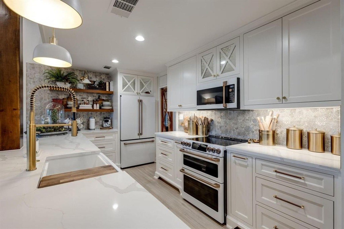 Bright kitchen with white cabinets, gold accents, and a spacious marble countertop fitted with a deep sink and modern fixtures.