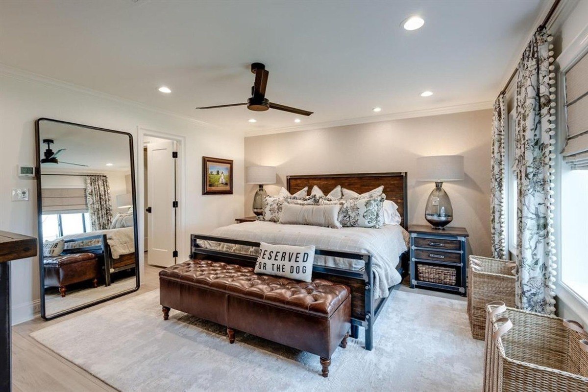 Bedroom layout features a cozy bed with layered pillows, a leather bench at the foot, and a full-length mirror leaning against the wall.