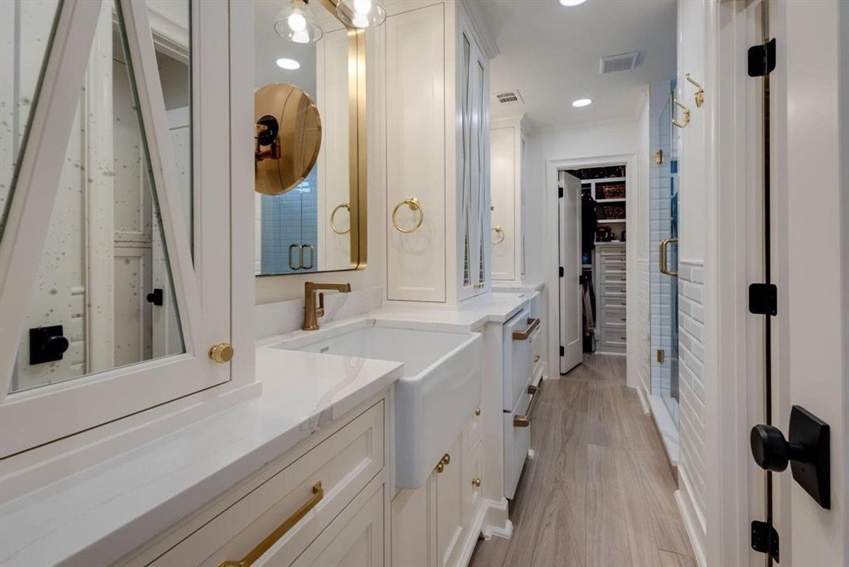 Bathroom vanity showcases a farmhouse-style sink, gold fixtures, and double mirrors with unique geometric framing.