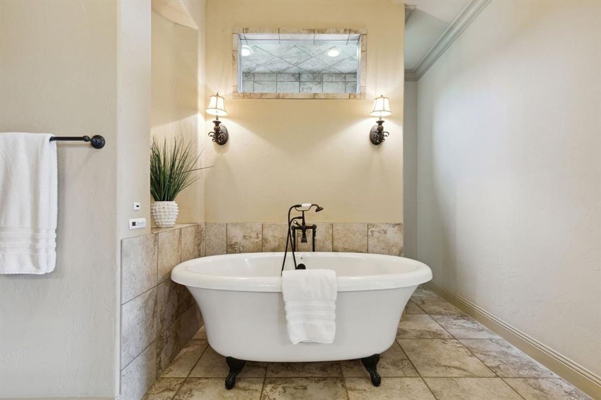 Freestanding bathtub with clawfoot legs, tile surround, and wall-mounted light fixtures.