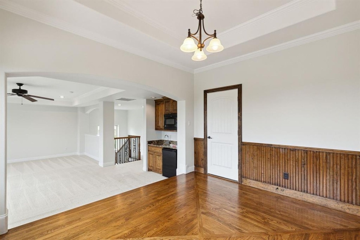 Secondary room with wood-paneled walls, hardwood floors, and access to a kitchenette.