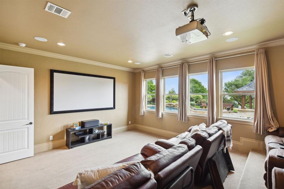 Media room with projector setup, leather recliners, and large windows offering pool views.