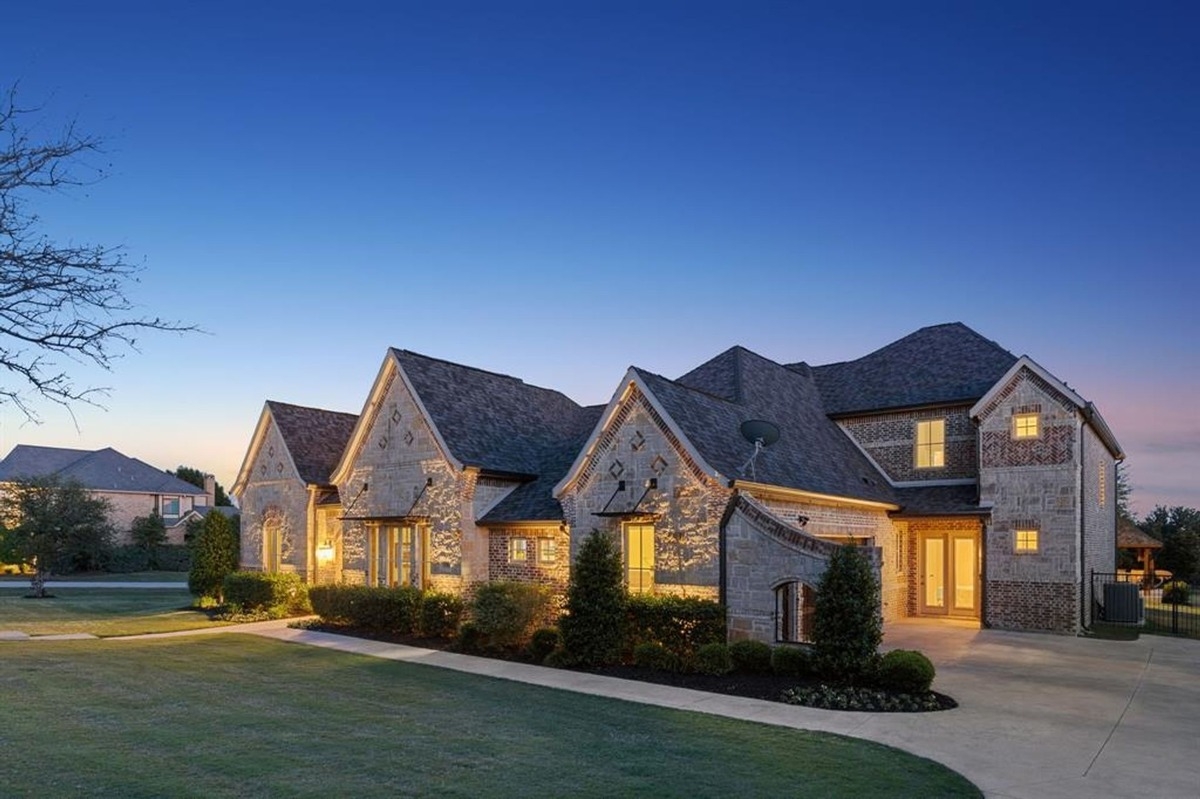 Side view of the same house showcasing a large driveway, shrubs, and windows illuminated in the evening.