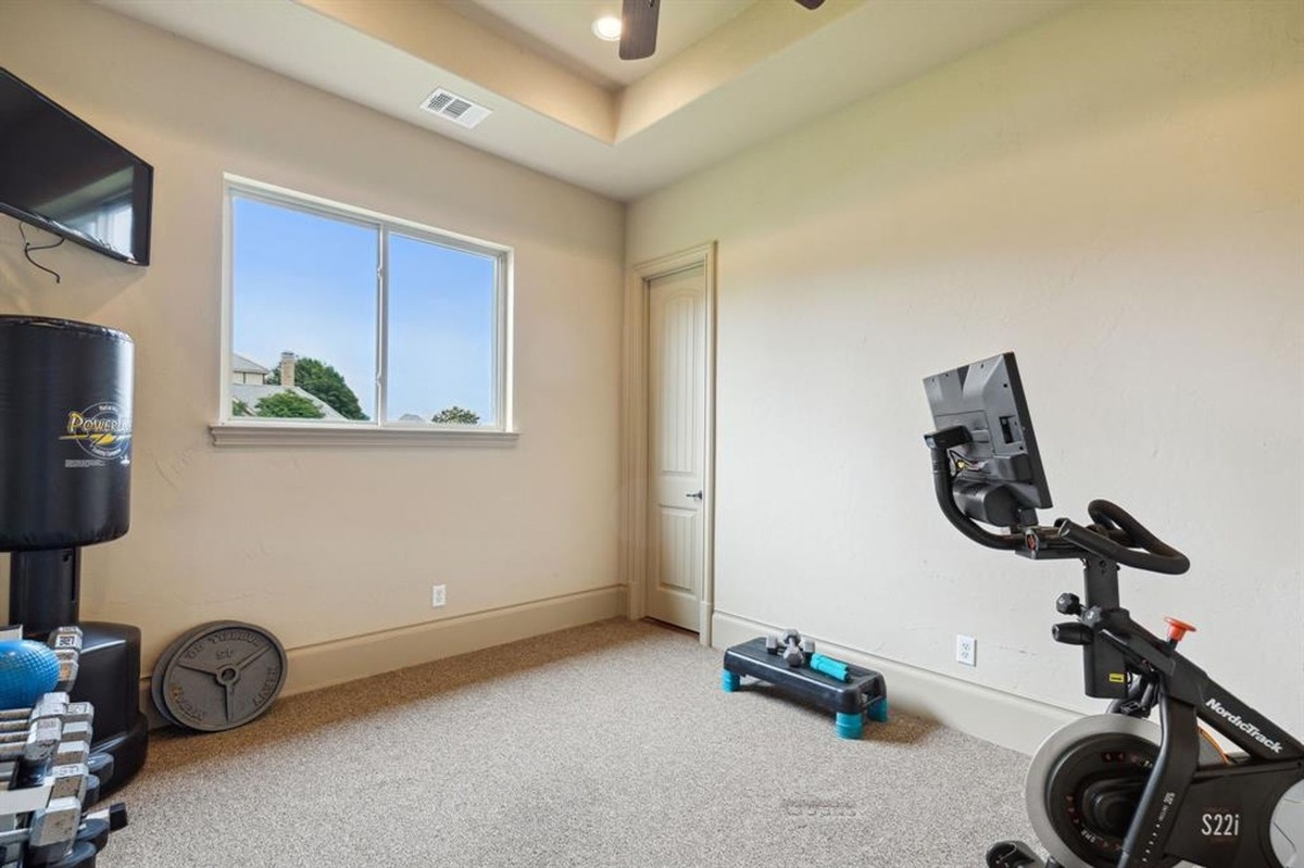 Exercise room with carpet flooring, wall-mounted TV, and workout equipment.