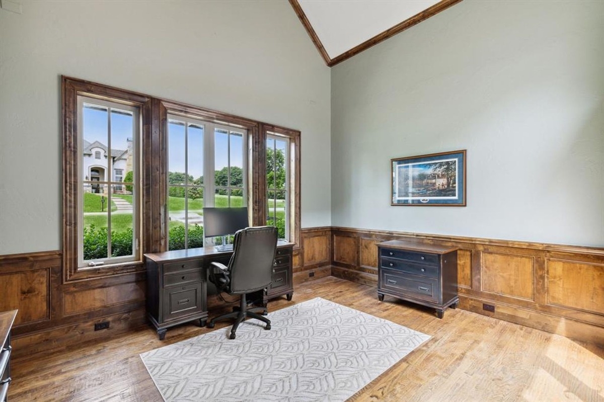 Office with wooden paneling and large windows overlooking a green lawn.