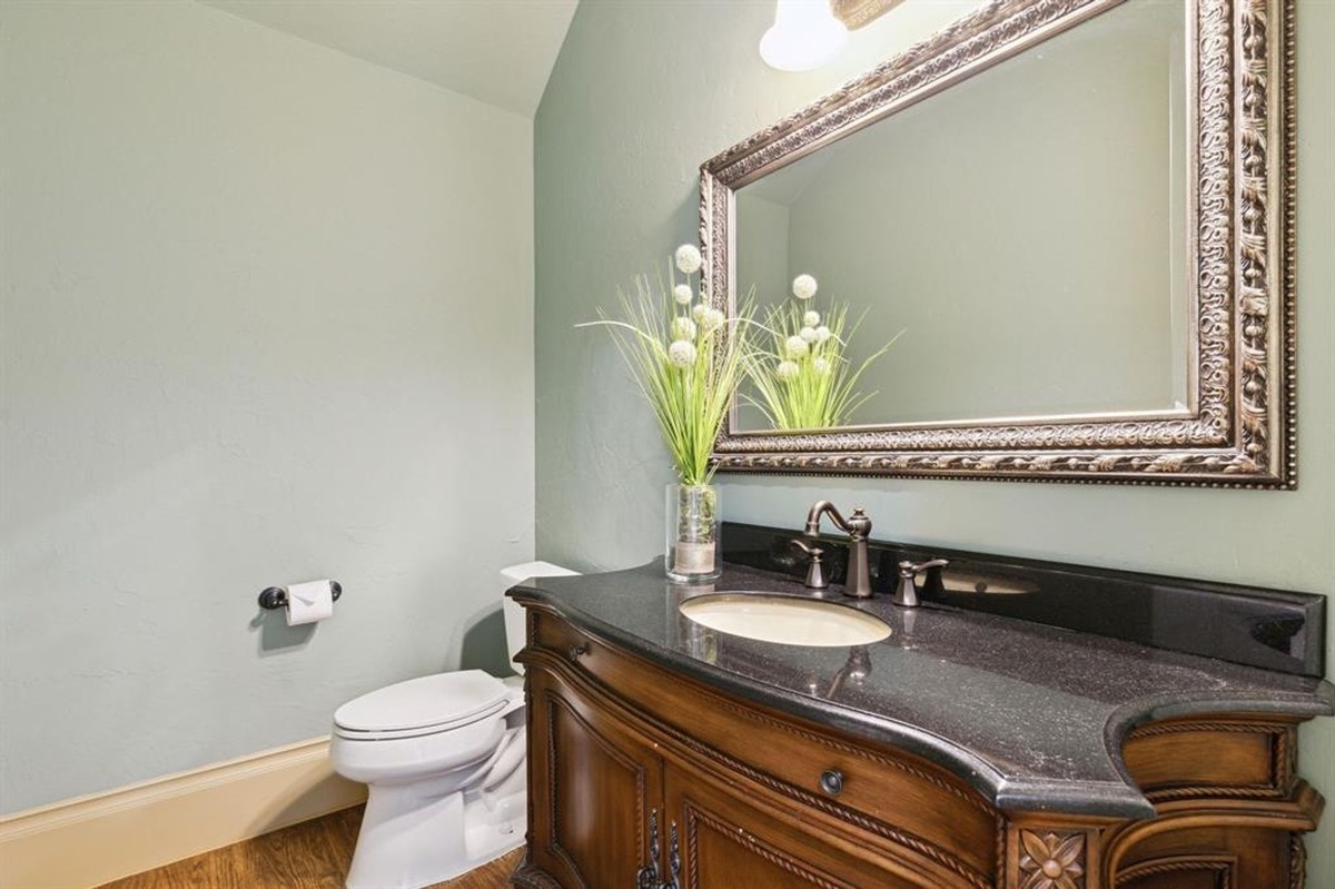 Bathroom with a decorative mirror, black countertop, and ornate wooden vanity.