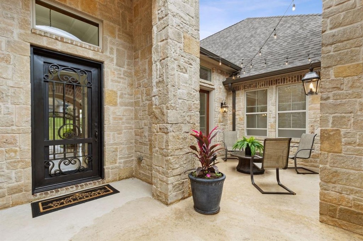 Courtyard entry with stone walls, iron door, potted plants, and patio seating.