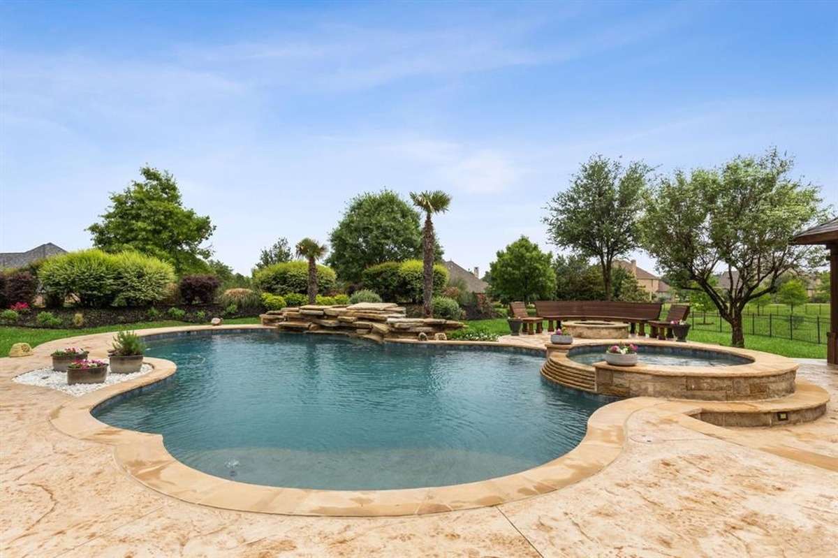 Pool with stone edging, waterfalls, and surrounding landscaped gardens.