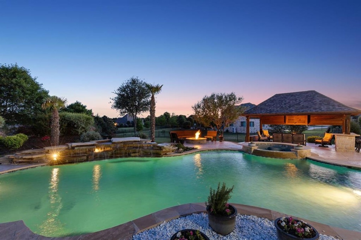 Evening view of the illuminated pool, firepit, and pavilion under a clear sky.