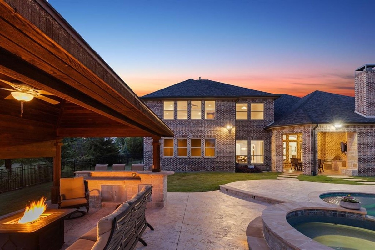 Brick exterior of a two-story home illuminated by sunset light with a spacious outdoor entertainment area and pool in the foreground.