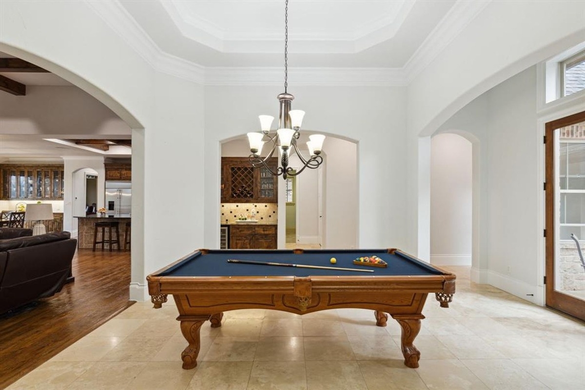 Interior room with a pool table under a central chandelier, flanked by open archways to adjacent spaces.