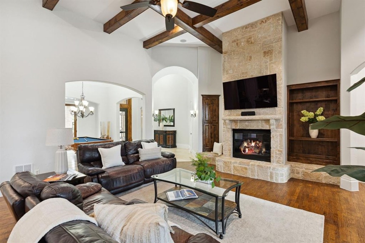 Living room featuring leather sofas, a stone fireplace, built-in shelves, and exposed wooden beams.