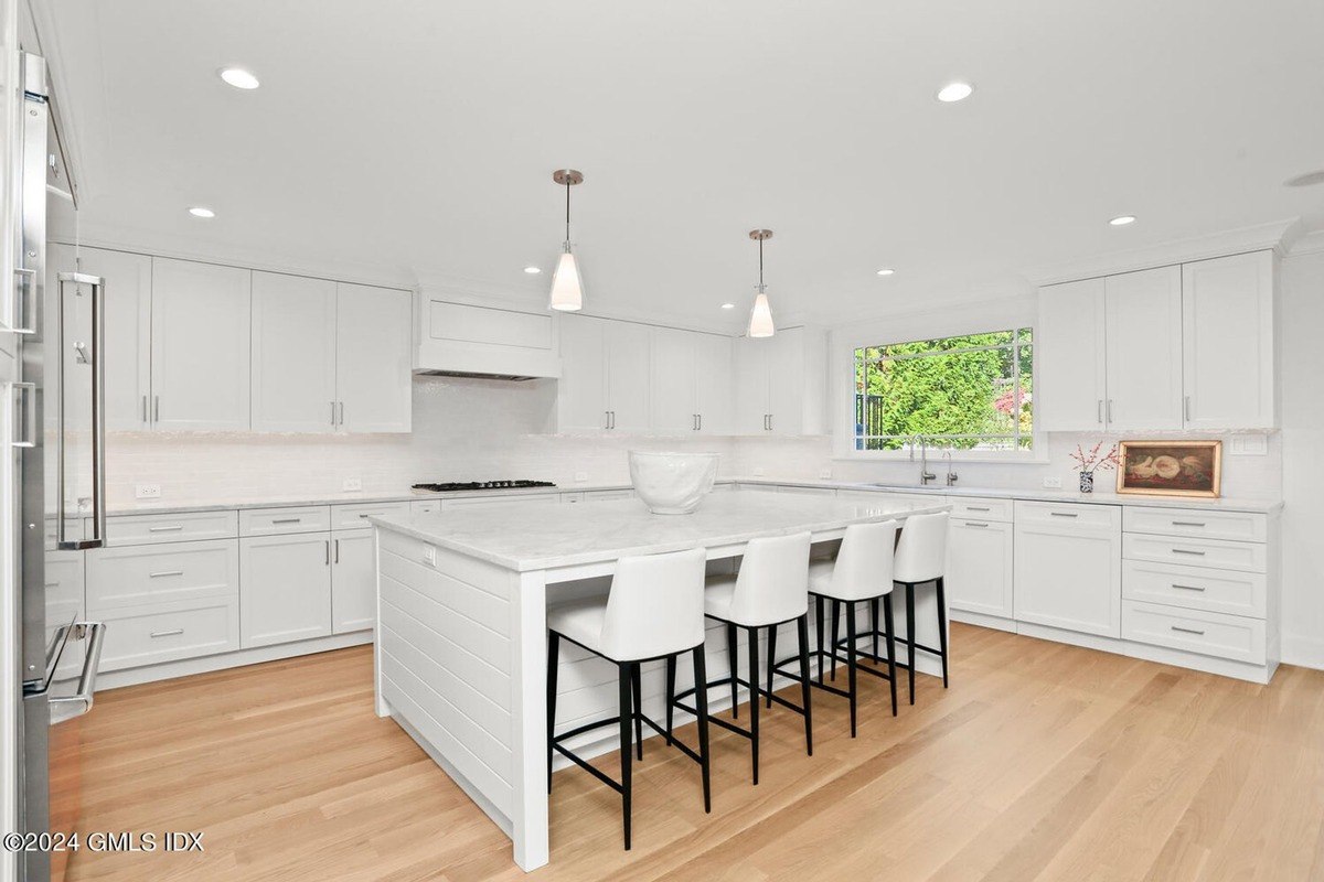 Kitchen has white cabinets, a large island, and hardwood floors.