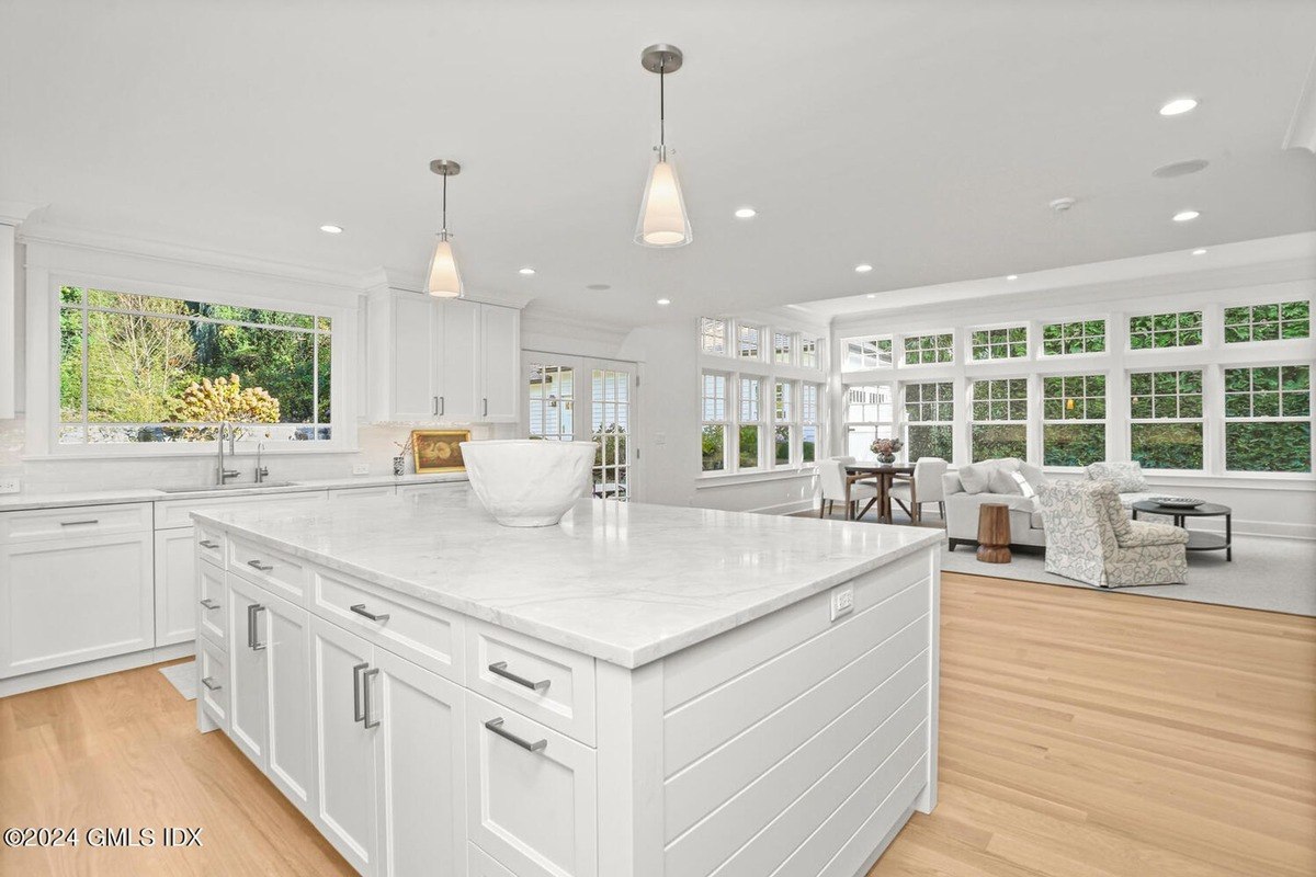 Kitchen has white cabinets, a large island, and a view of a living area.