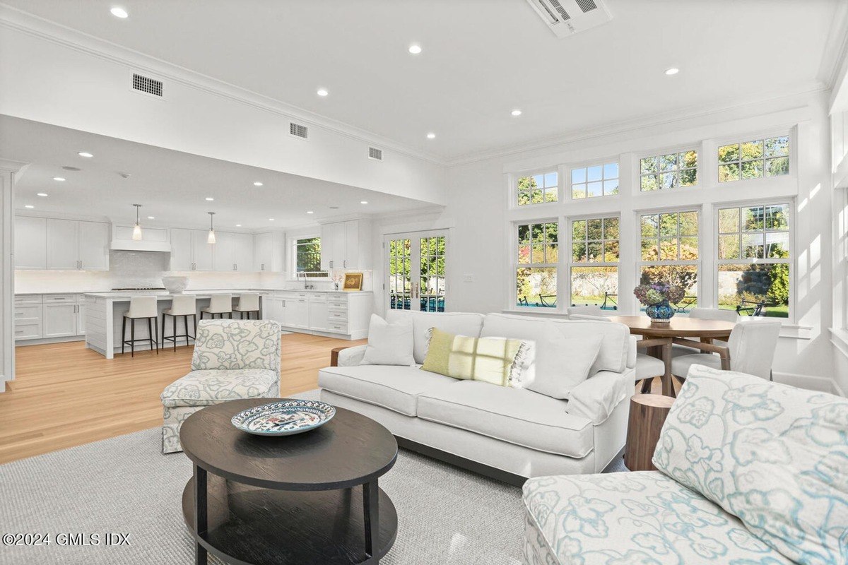 Living room has white sofas and a view of a kitchen with an island.