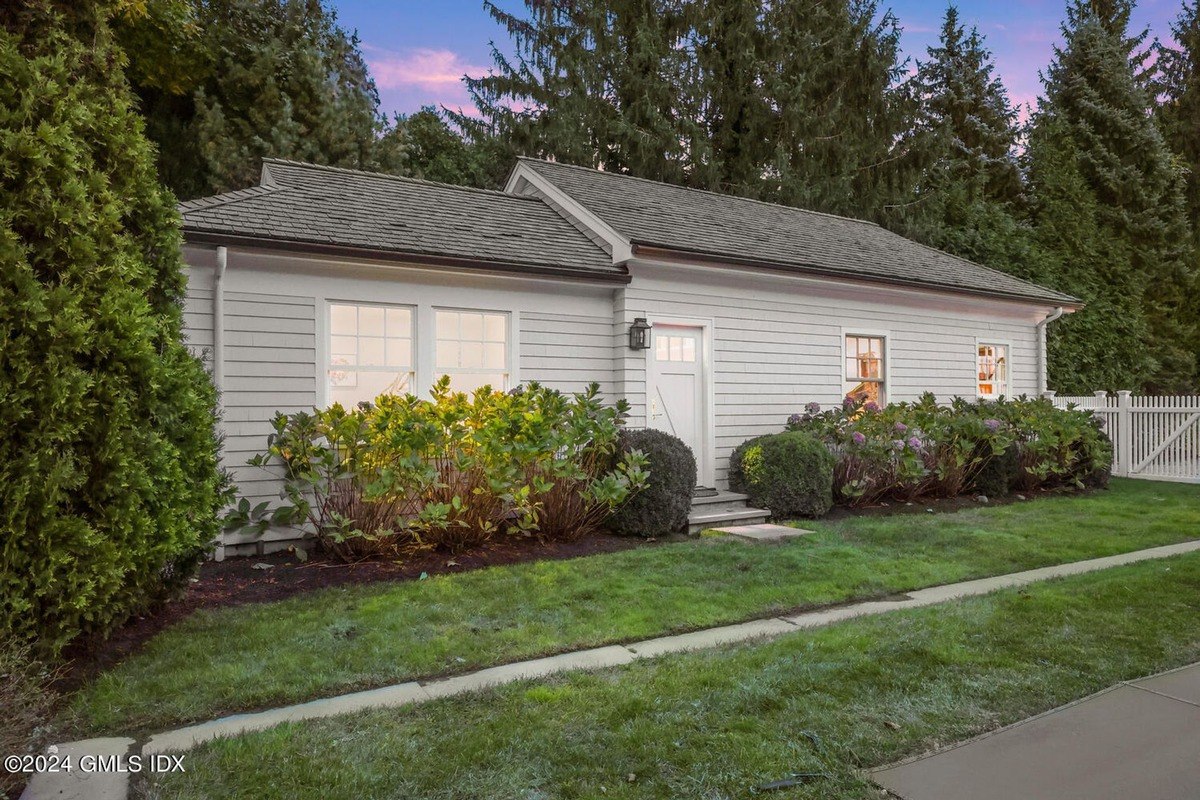 Small white house has a gray roof and is surrounded by landscaping.