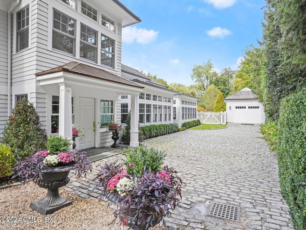 House has a white exterior, stone driveway, and landscaping.