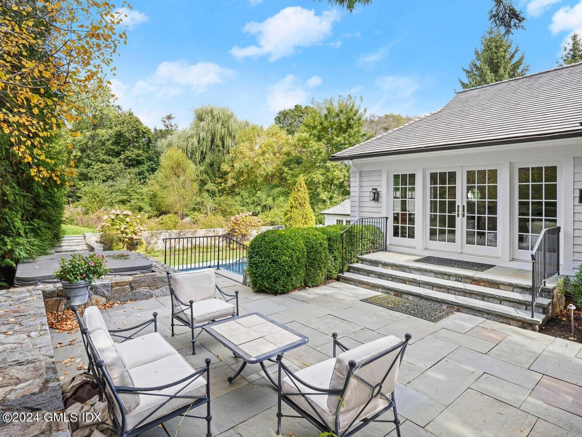 Patio has seating, a stone wall, and a view of a pool and woods.