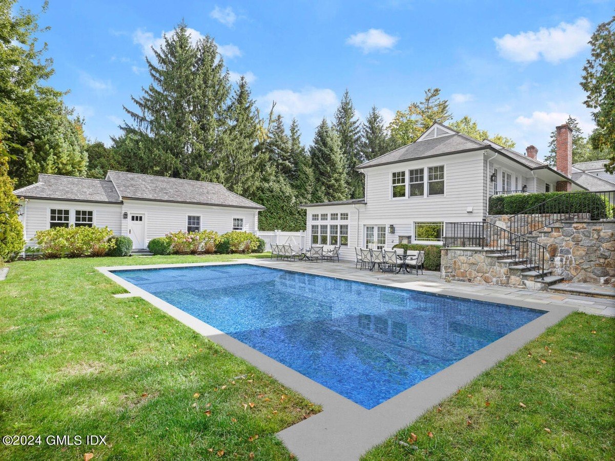 Backyard has a swimming pool, patio furniture, and a white house.