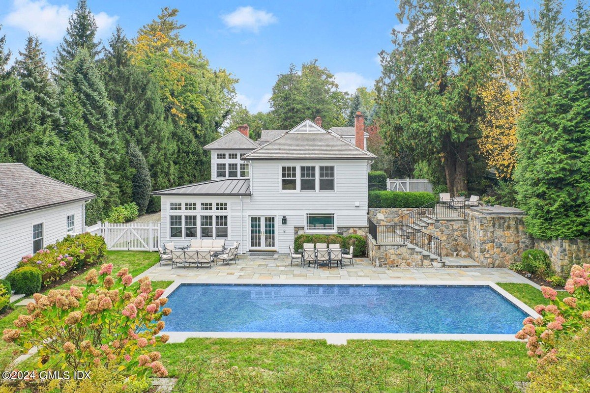 Backyard has a swimming pool, patio furniture, and a white house surrounded by trees.