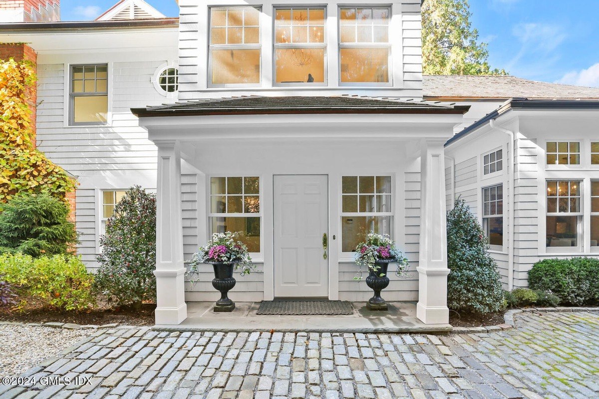 White house has a front entrance with two large urns and a brick walkway.