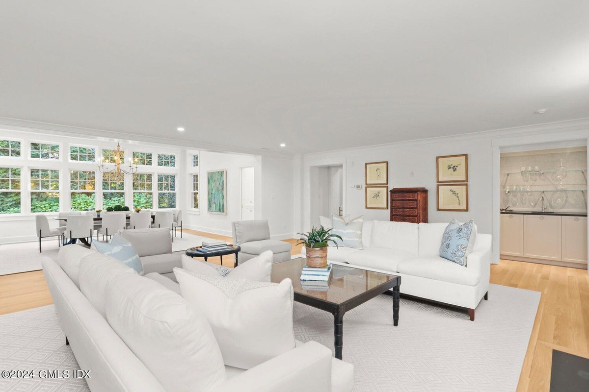 Living room has white sofas, a large window, and hardwood floors.