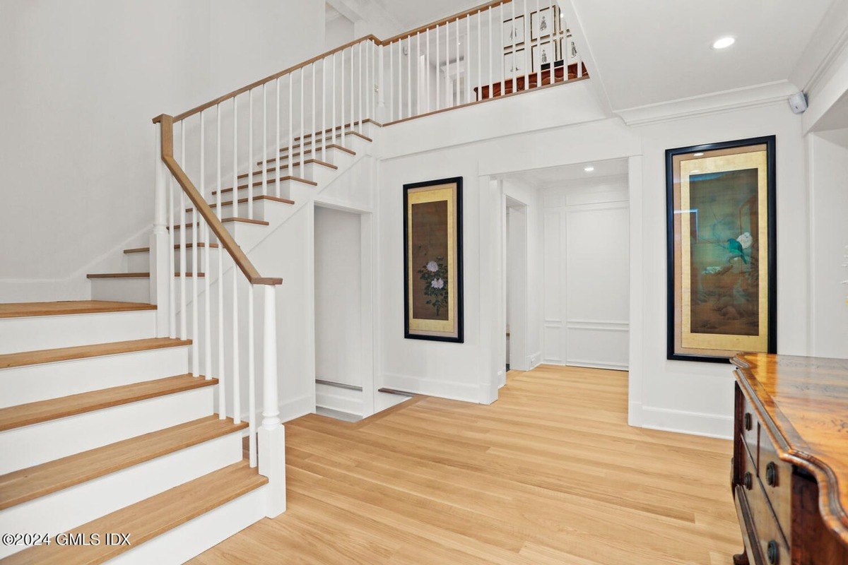 Entryway has hardwood floors, white staircase, and artwork on walls.