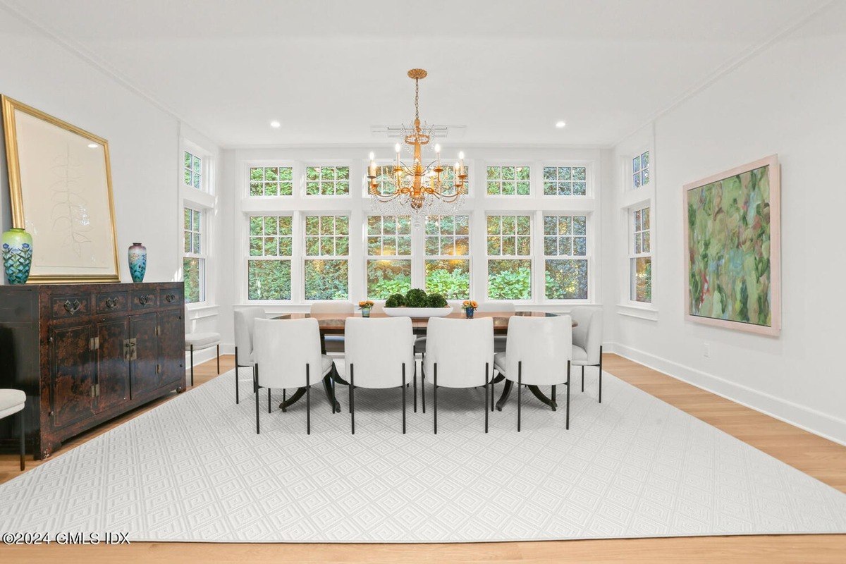 Dining room has white chairs, a large window, and a chandelier.