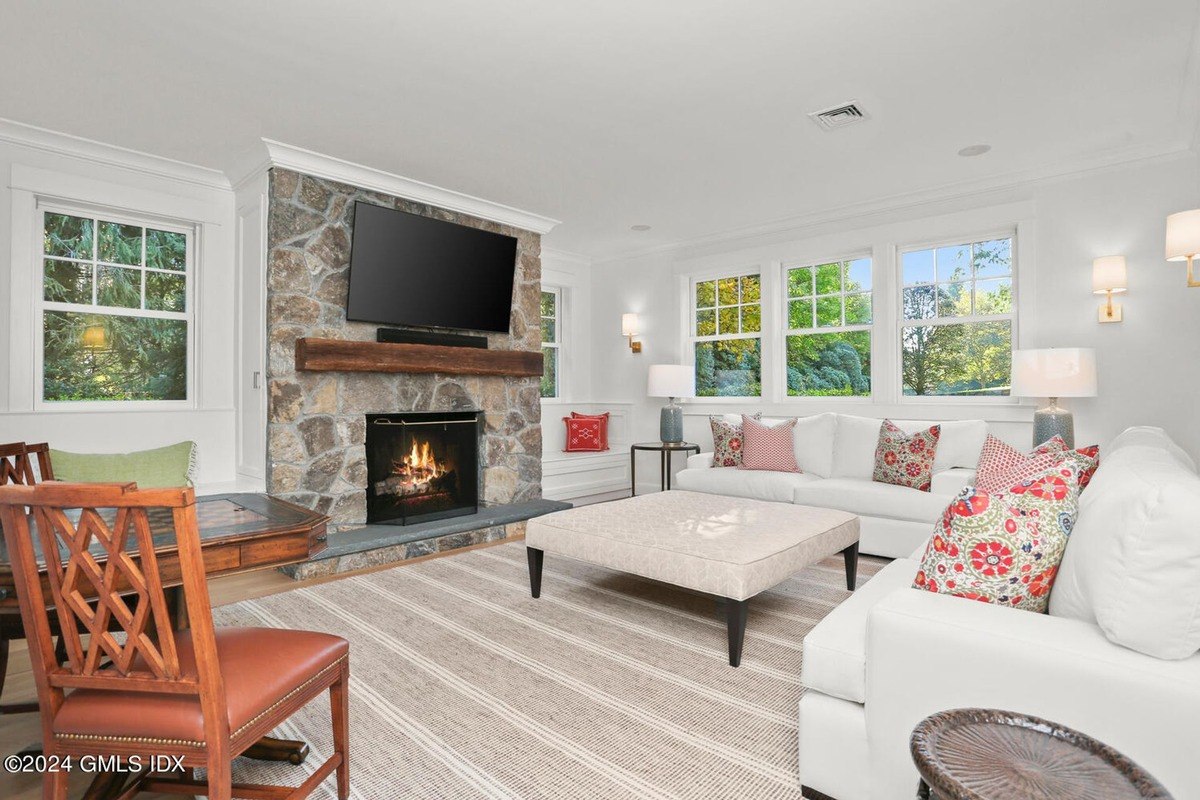 Living room has white sofas, a stone fireplace, and large windows.