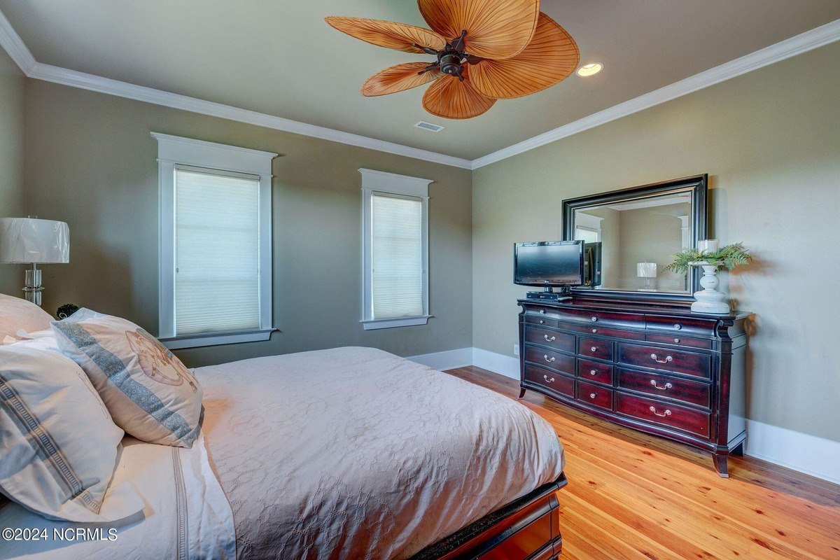 Bedroom has hardwood floors, ceiling fan, and dresser.