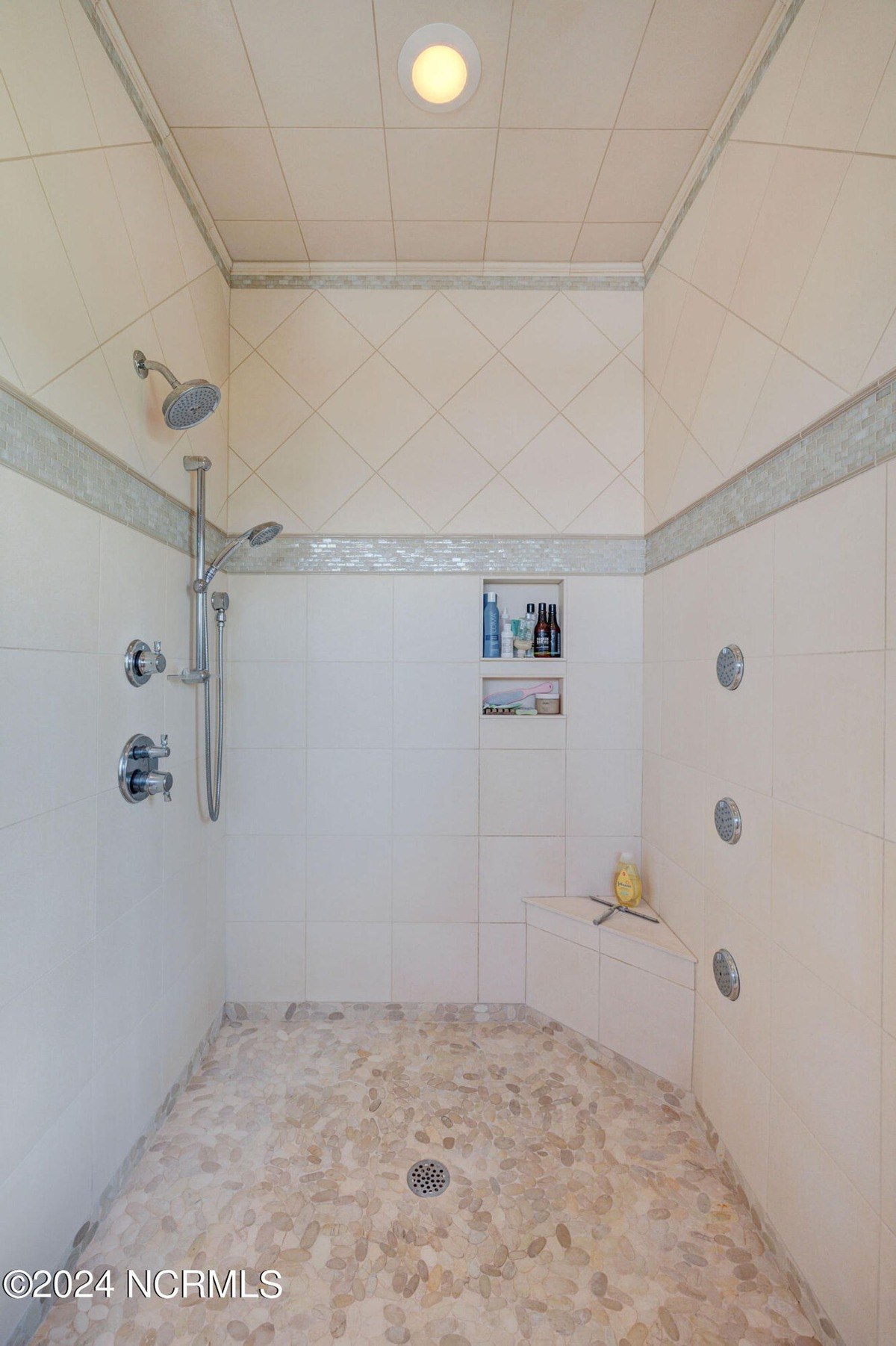 Shower has tiled walls, stone floor, and built-in shelves.