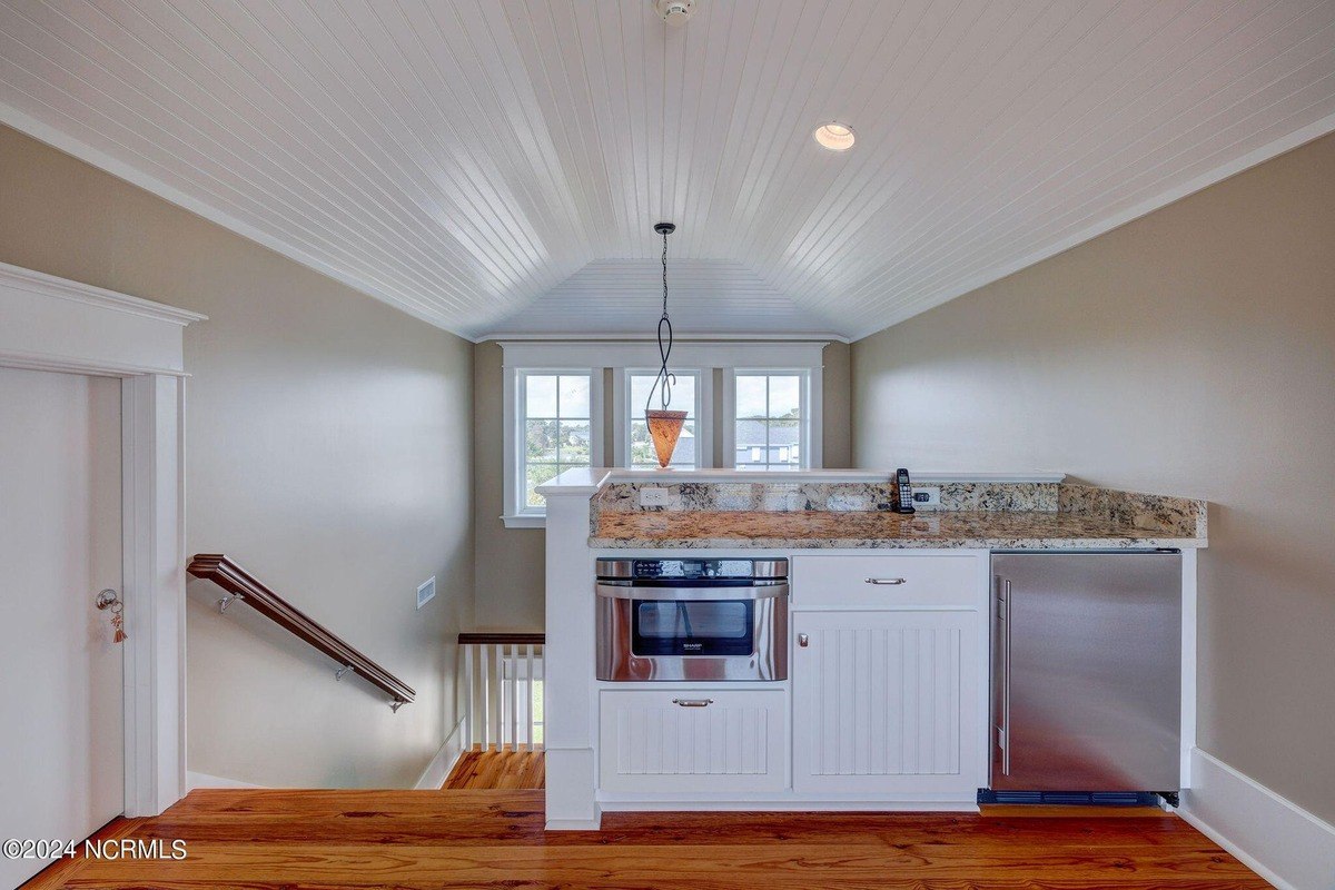 Wet bar has white cabinets, granite countertop, and built-in appliances.