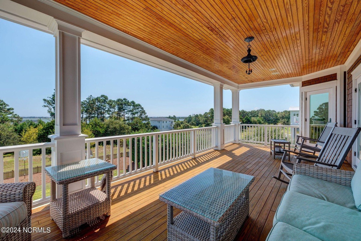 Porch has wood flooring, wicker furniture, and railing overlooking water.