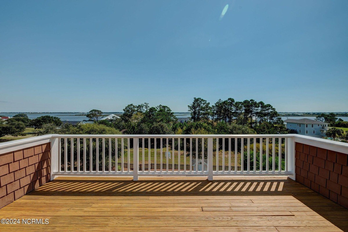 Deck has wood flooring, white railing, and water view.